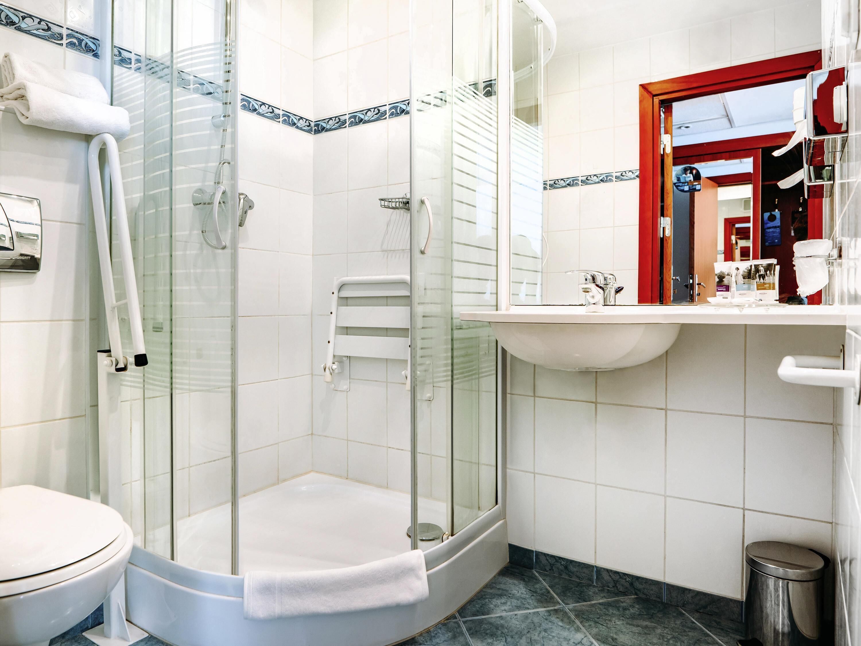 Un baño con ducha de vidrio, inodoro blanco, lavamanos con espejo y puerta con marco rojo.