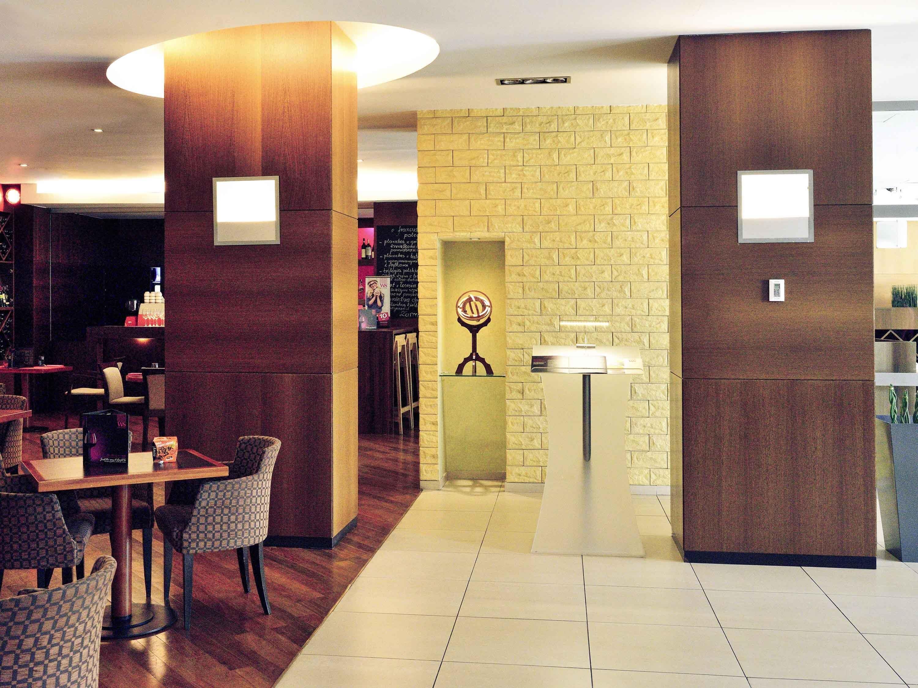 A hotel lobby with a reception desk, a seating area with patterned chairs, and a wall with a brick-like texture.