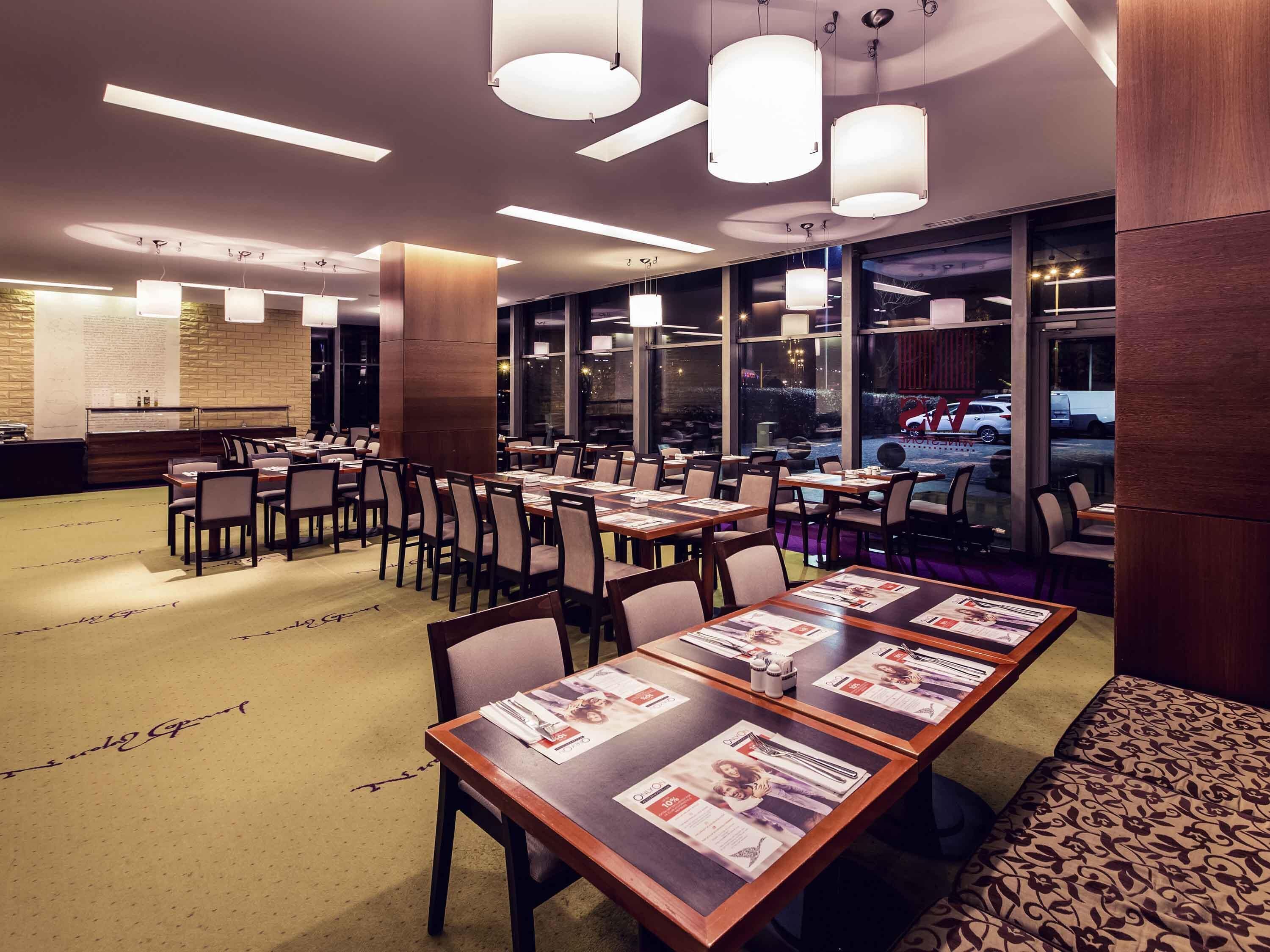 A restaurant with multiple tables and chairs, large windows, and hanging pendant lights.