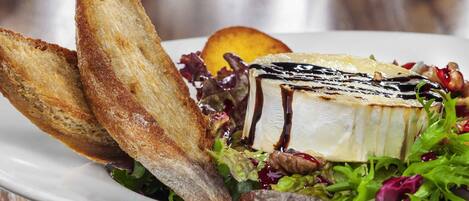 Un plato de comida con un sándwich de queso a la plancha, un trozo de queso con salsa de chocolate y una ensalada.