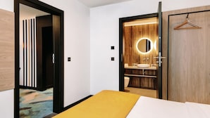 A hotel room with a bed, a bathroom with a wooden vanity, and a hanging coat rack. - Hotel Mercure Torun Centrum (Torun)
