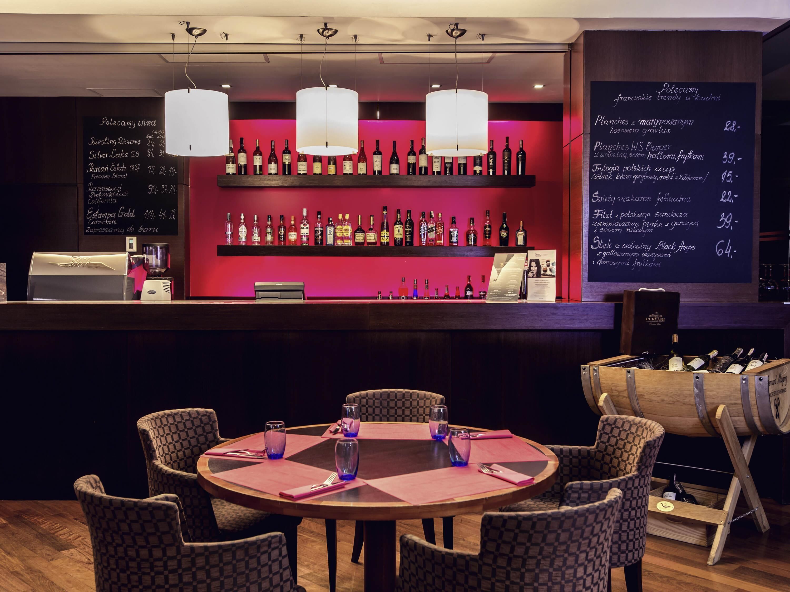 A bar area with a selection of bottles, a menu board, and a round table with chairs.