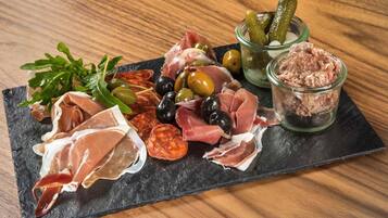 Une planche de charcuterie comprenant différentes sortes de viandes, des olives, des cornichons et des légumes verts, le tout présenté sur une ardoise.