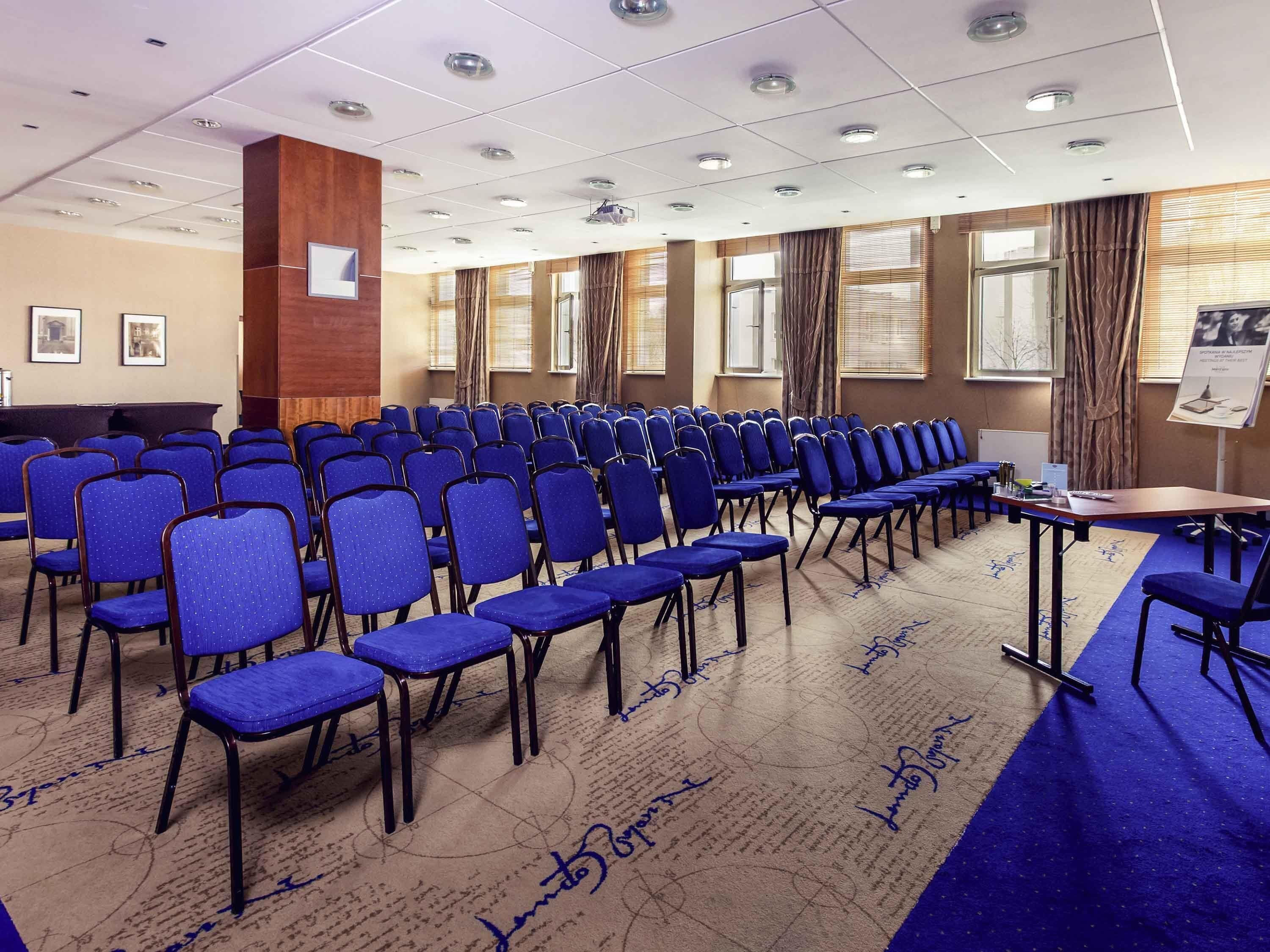 A conference room with rows of blue chairs, a podium, and a carpet with signatures.