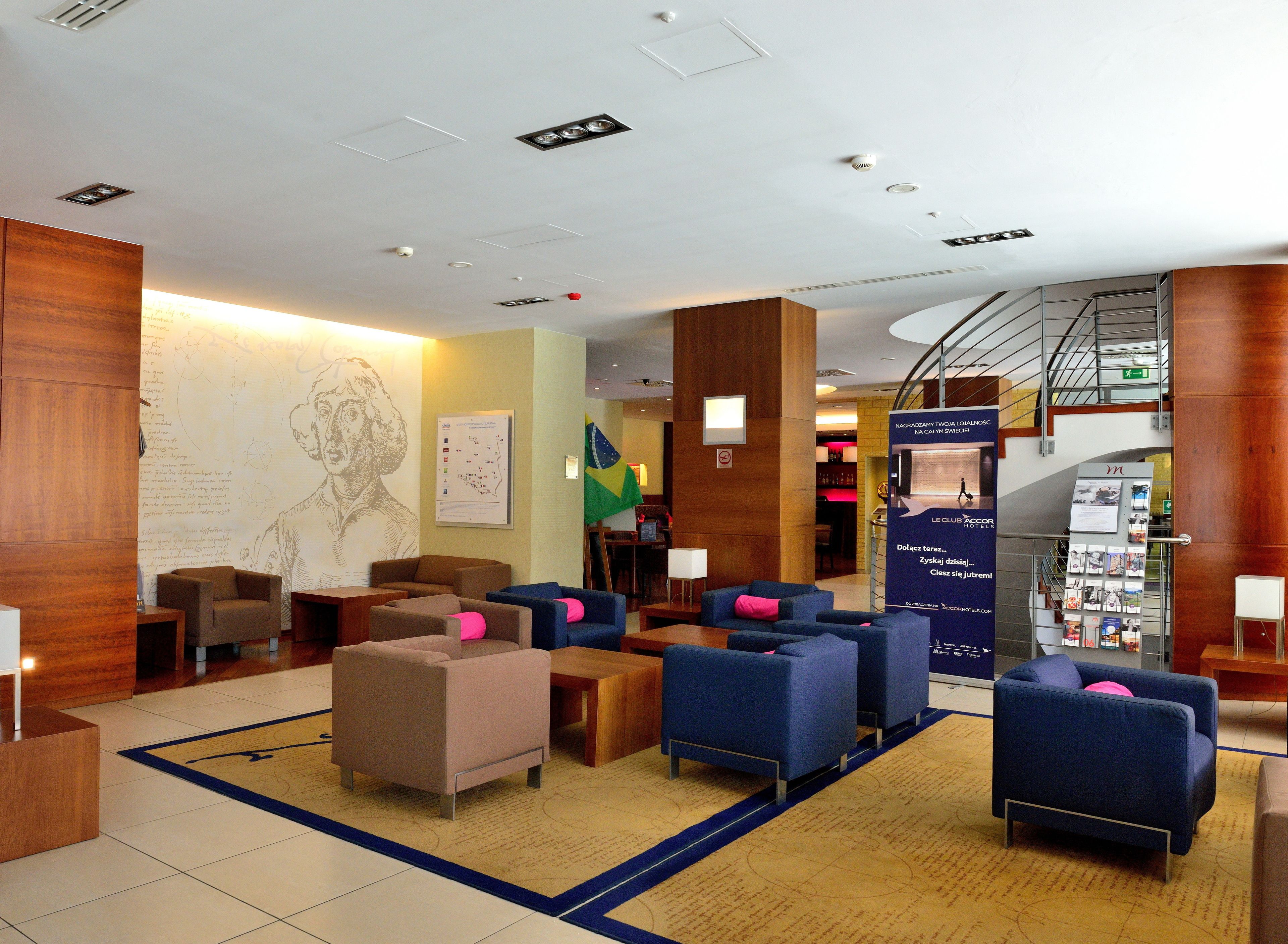 A hotel lobby with seating areas, a reception desk, a map on the wall, and a staircase.