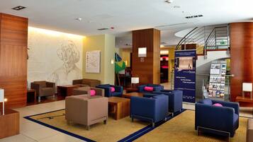 A hotel lobby with seating areas, a reception desk, a map on the wall, and a staircase.
