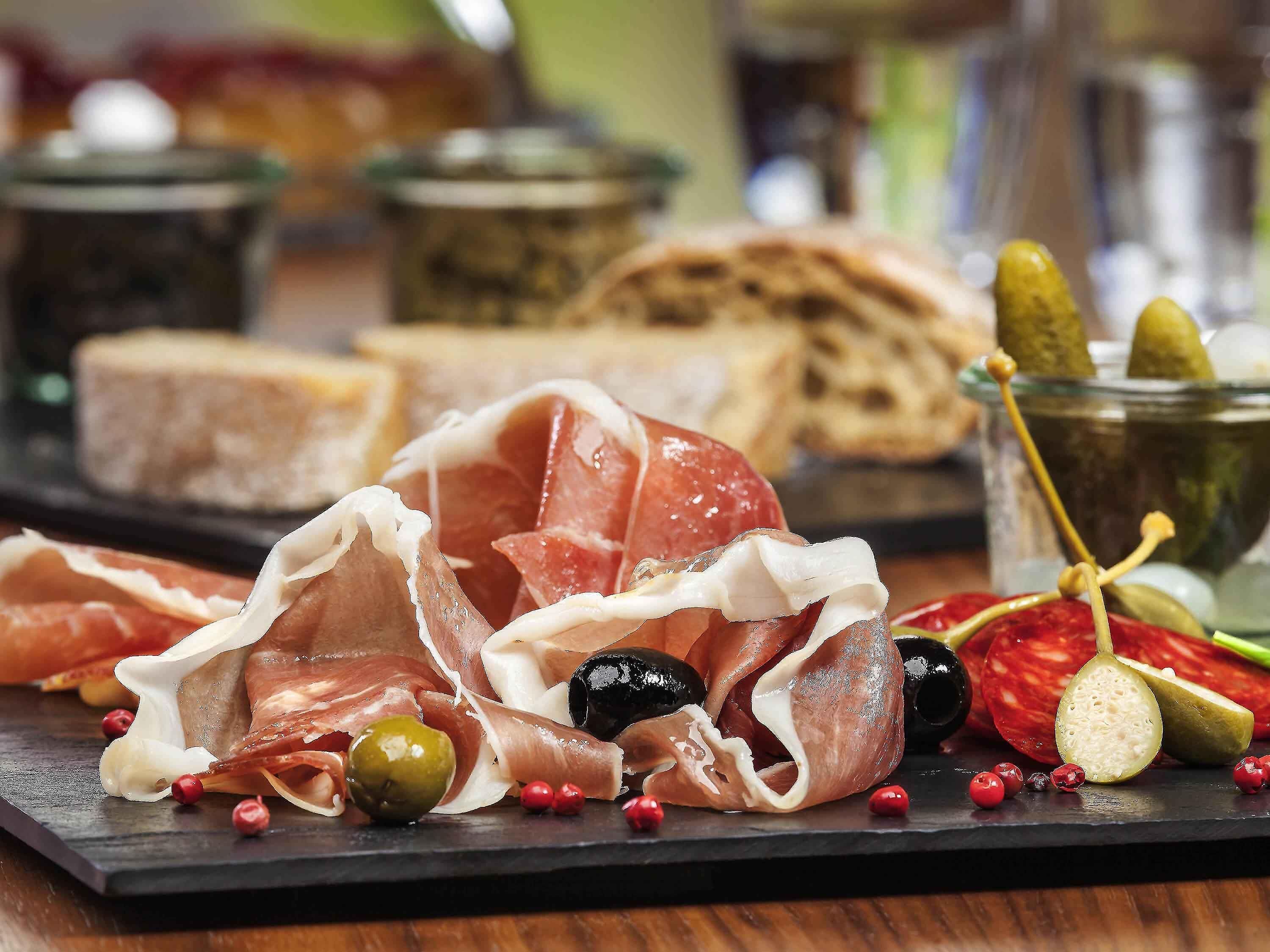 Una tabla de embutidos con diferentes carnes, aceitunas y pepinillos.