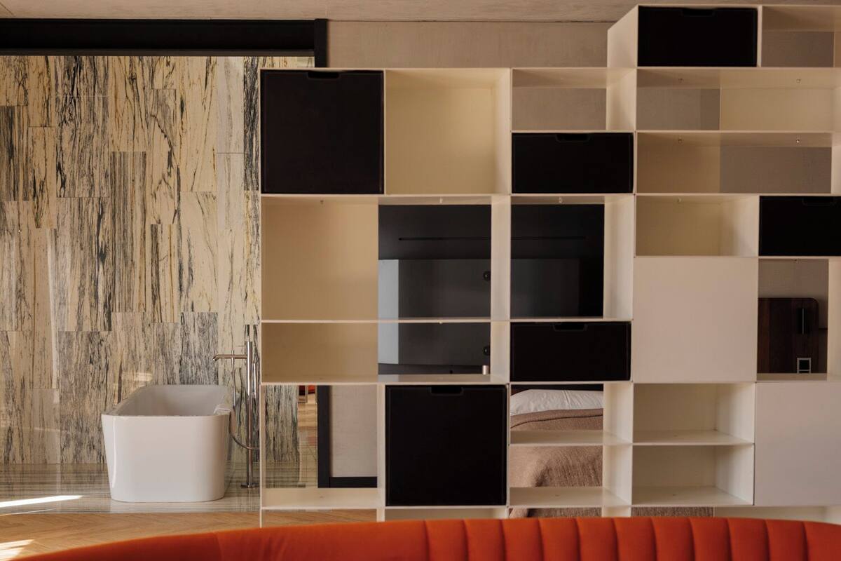 Una sala de estar moderna con un sofá naranja curvo, una mesa de centro de vidrio y una pared con diseño de mármol.