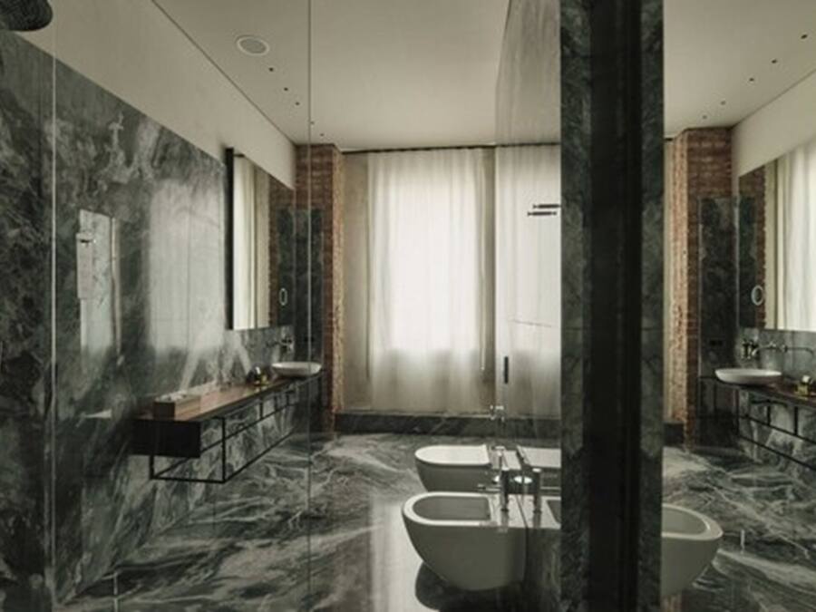Une salle de bain moderne avec des murs en marbre, deux lavabos, une baignoire et un grand miroir.