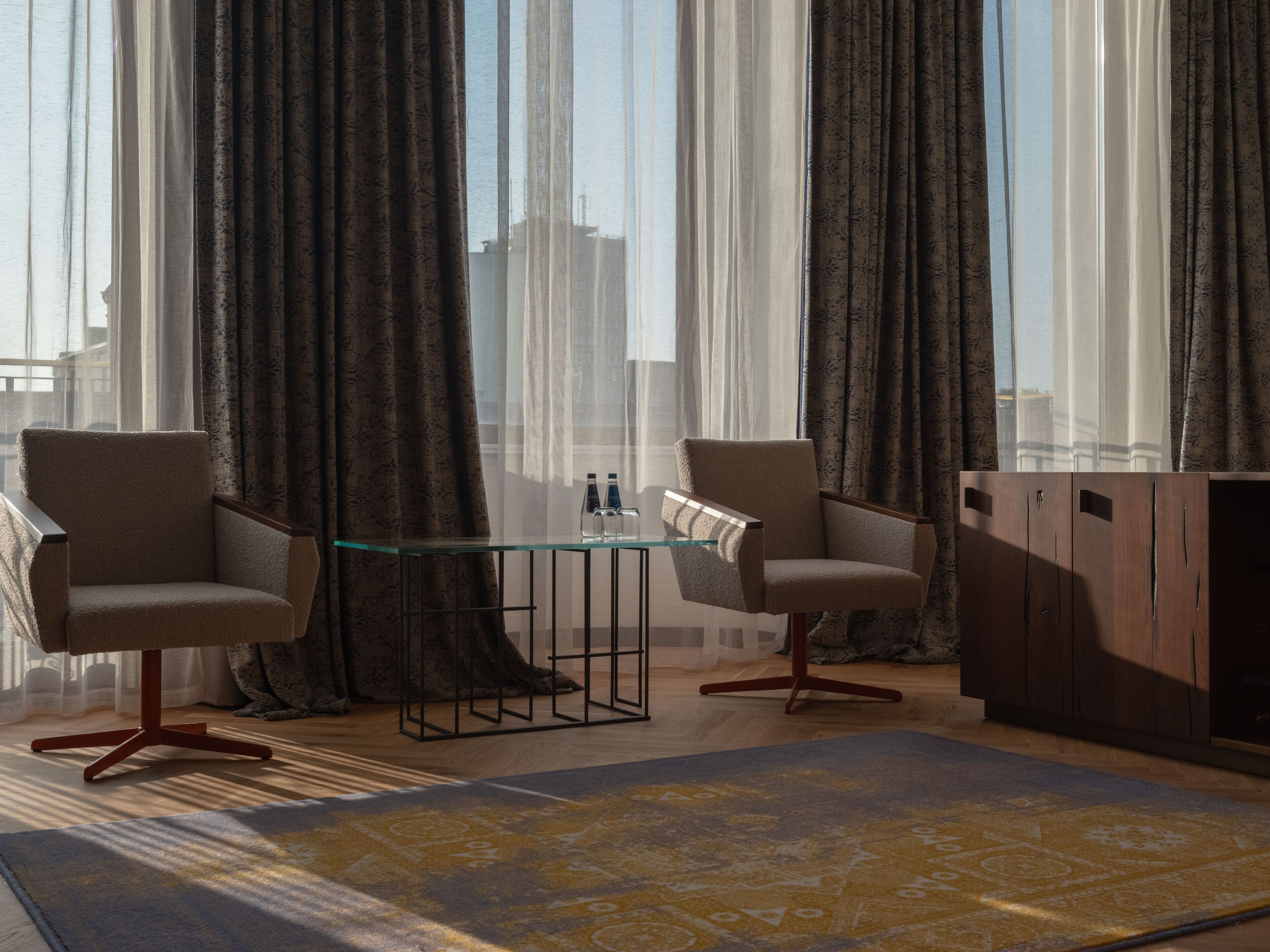 A modern living room with two armchairs, a glass coffee table, and a wooden cabinet.