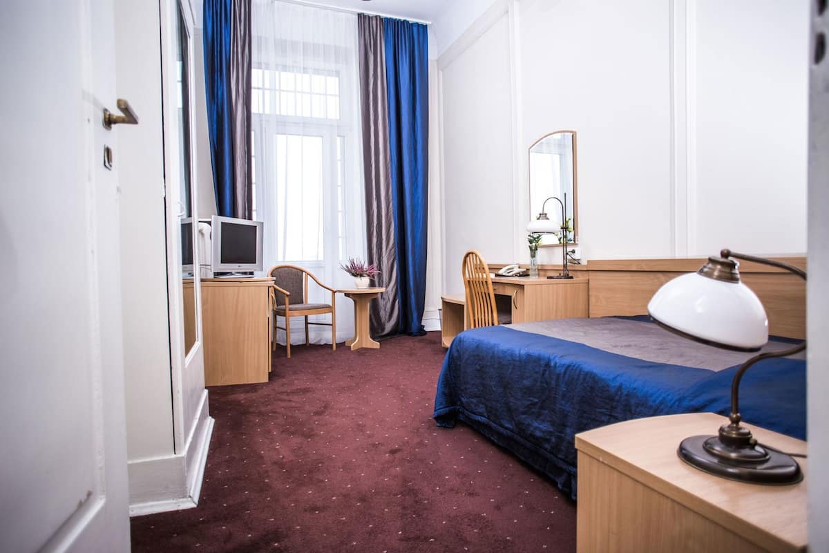 Una habitación de hotel con cama, escritorio, silla, televisor y espejo.