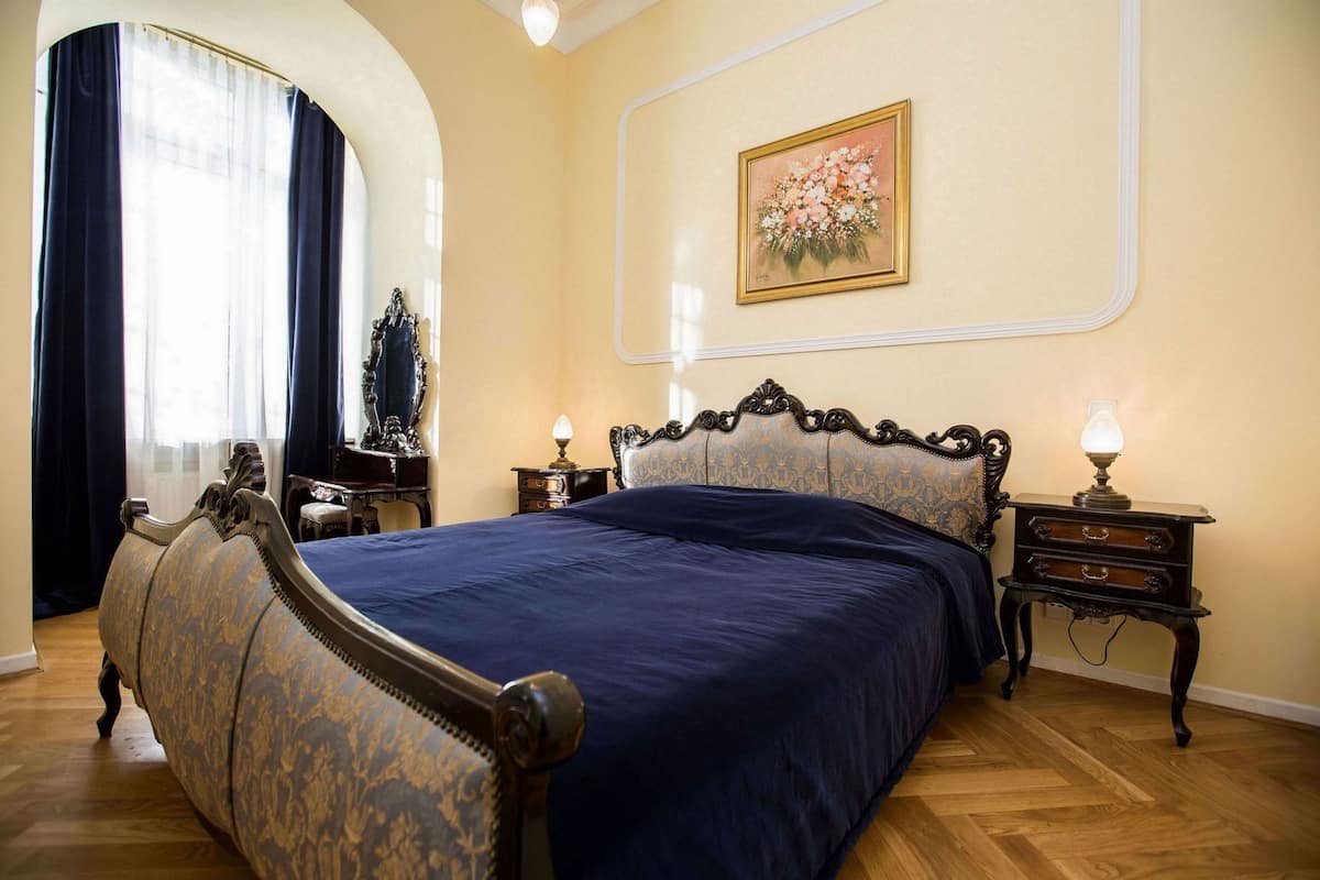 Un dormitorio con una cama grande, dos mesitas de noche, un espejo y un cuadro con motivos florales en la pared.