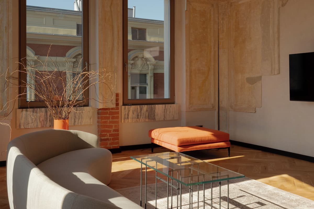 Una sala de estar moderna con ventanas amplias, un sofá, una mesa de centro de vidrio y un televisor de pantalla plana montado en la pared.