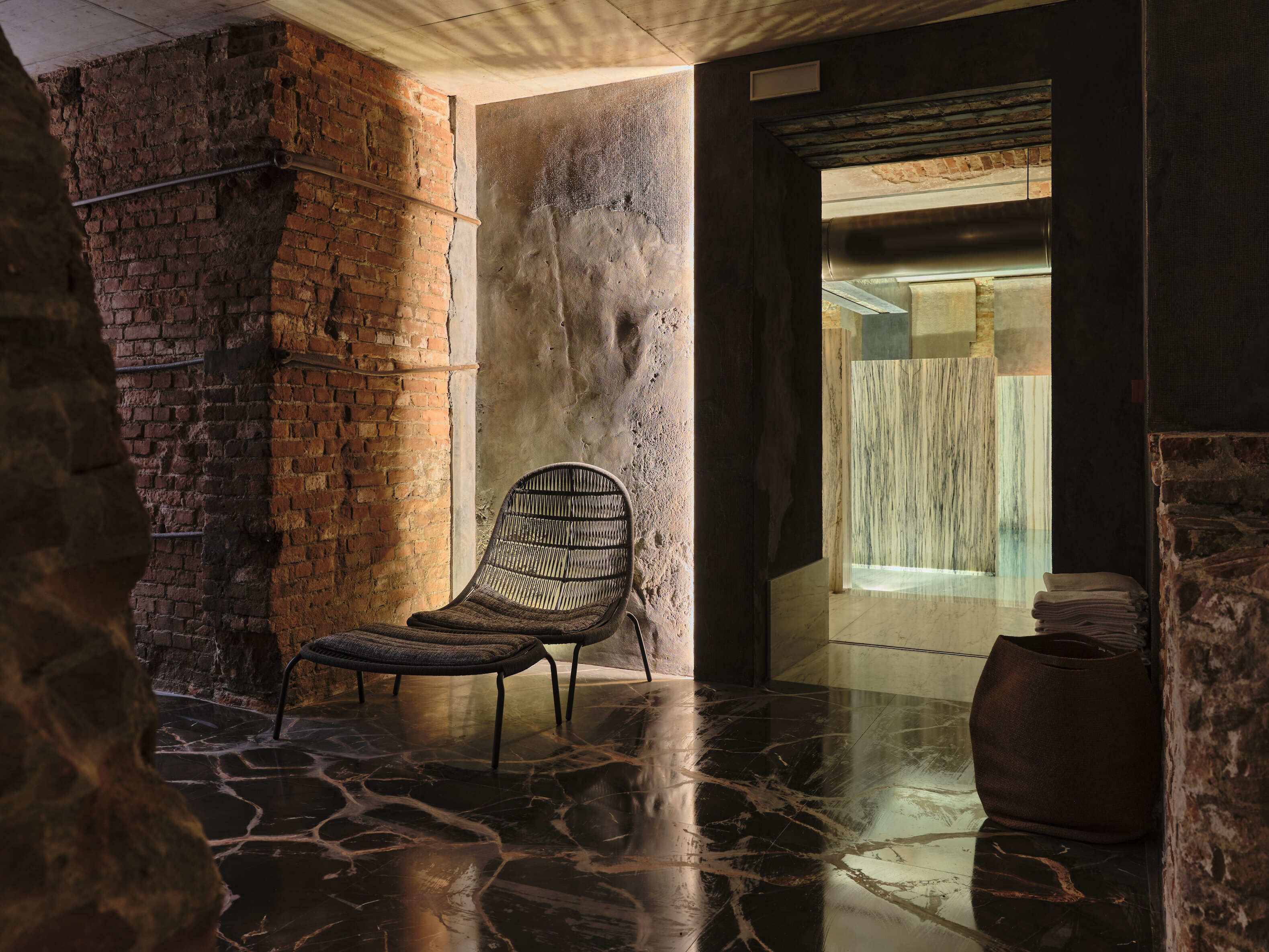 A room with a brick wall, a chair, and a marble floor.