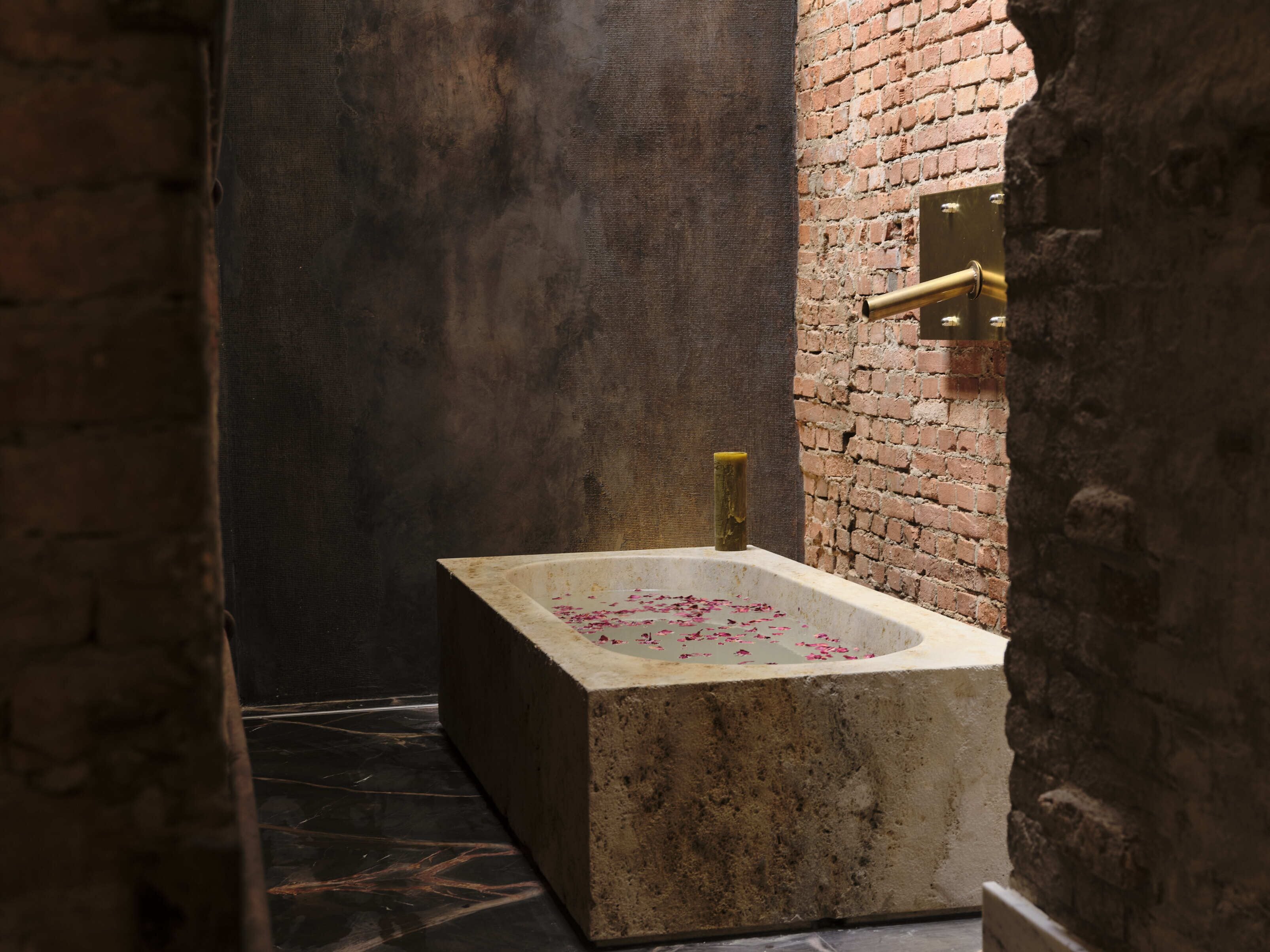 A bathroom with a rectangular bathtub, a brick wall, and a metal faucet.