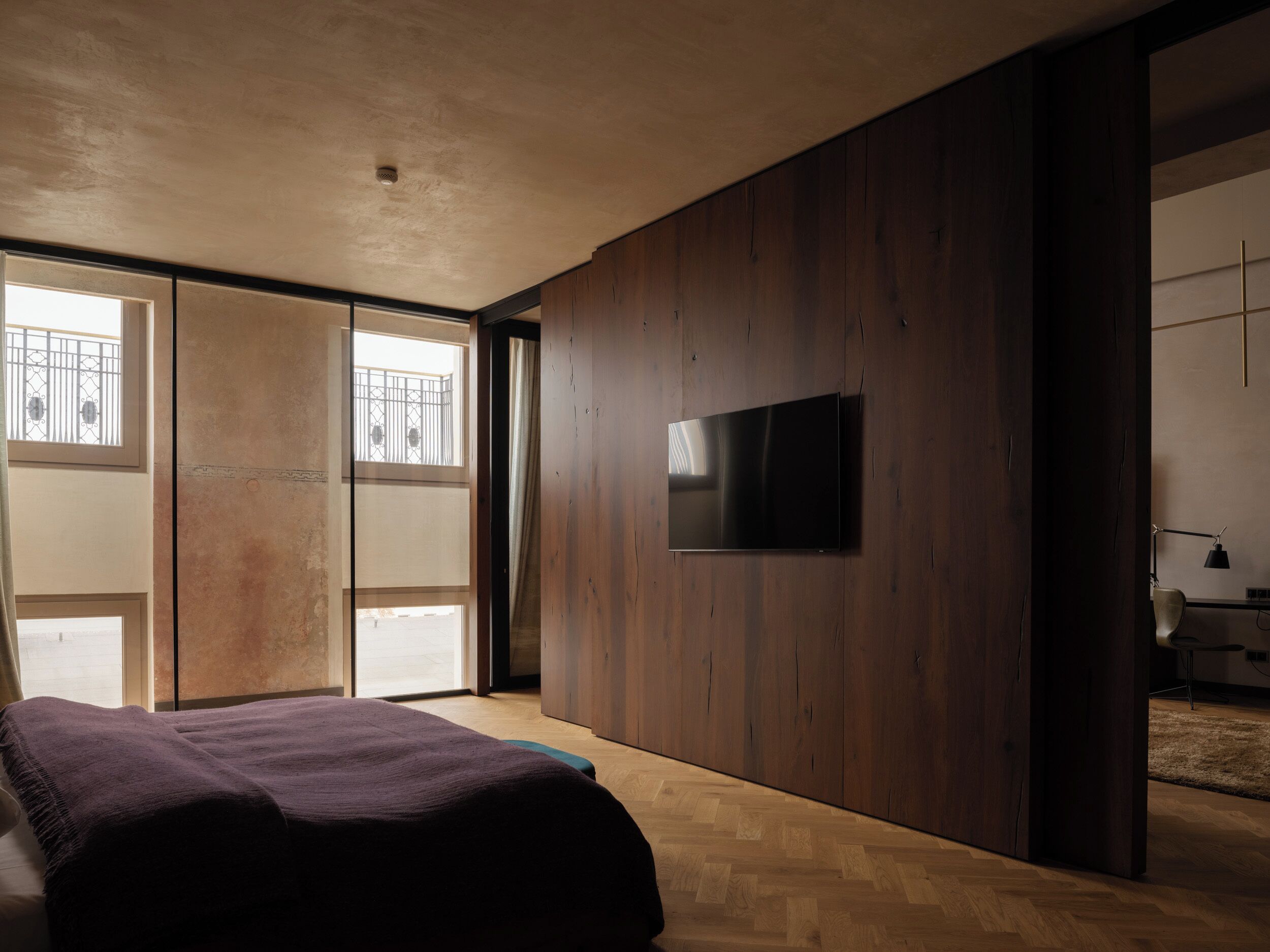 Une chambre moderne avec un grand lit, un téléviseur à écran plat fixé au mur et une porte coulissante donnant sur un balcon.