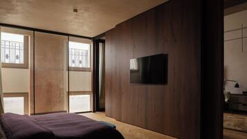 Une chambre moderne avec un grand lit, un téléviseur à écran plat fixé au mur et une porte coulissante donnant sur un balcon.