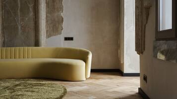 A room with a yellow sofa, a green rug, and a wooden floor.