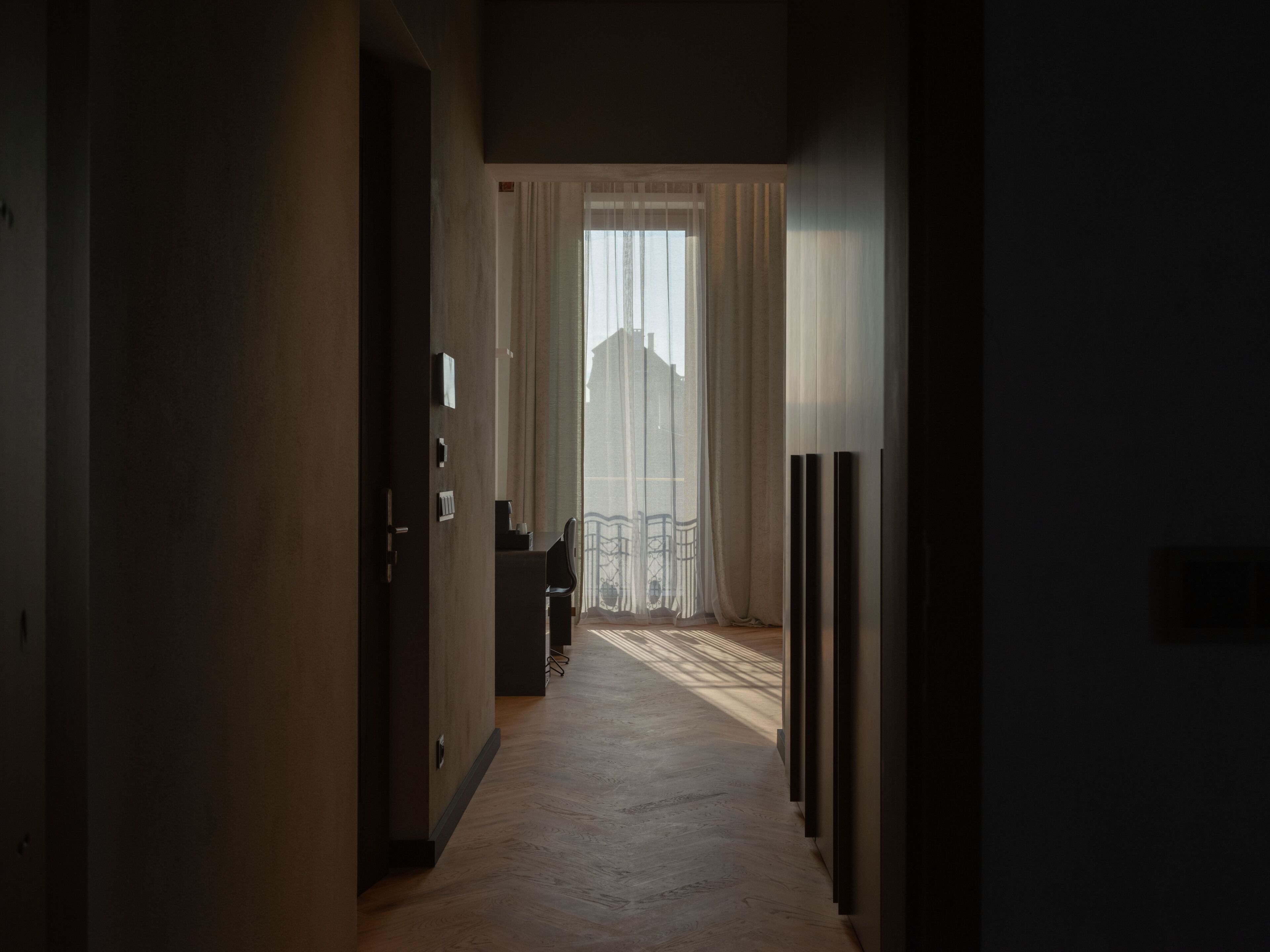 Un pasillo estrecho con suelo de madera que conduce a una habitación con un ventanal y cortinas.