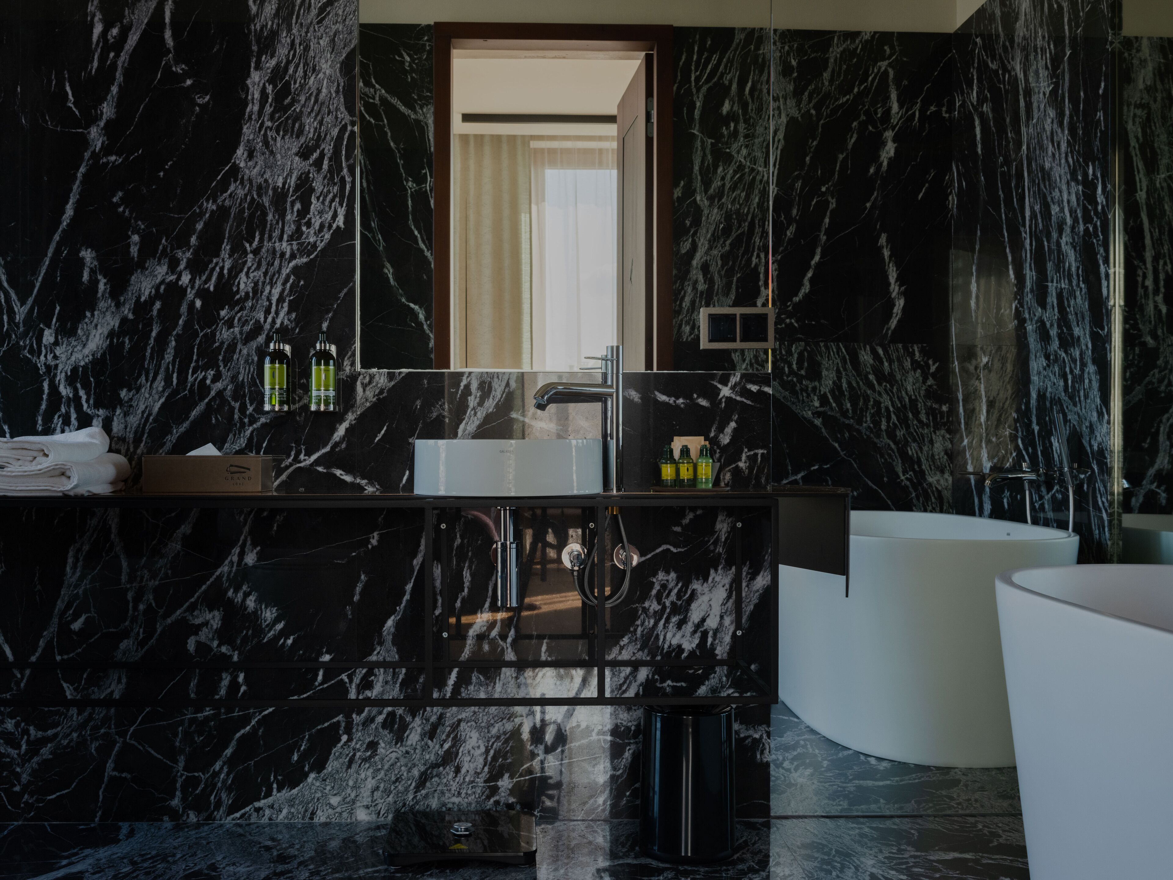 A modern bathroom with a marble backsplash, a white sink, and a freestanding bathtub.