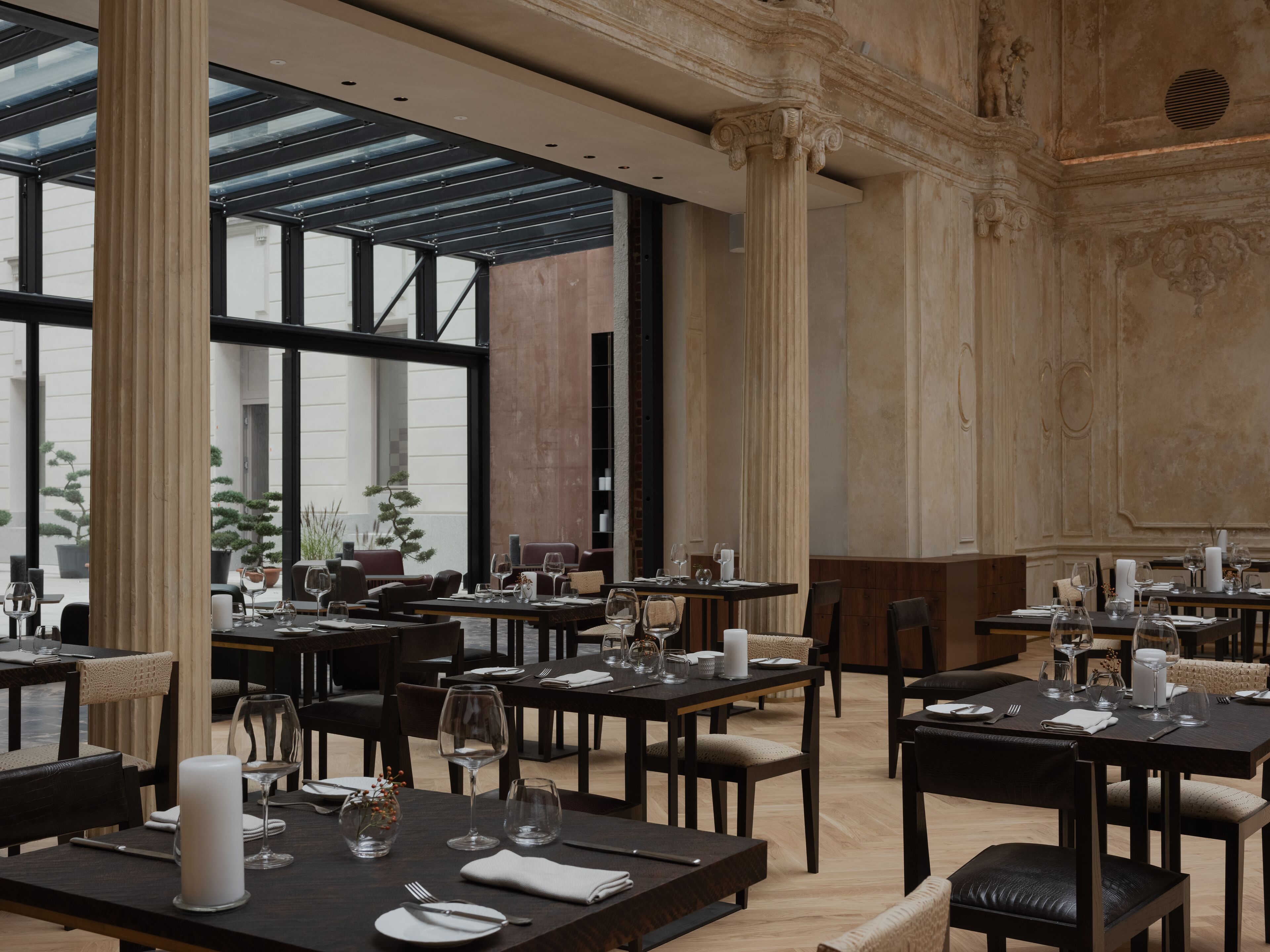 Un restaurante con varias mesas dispuestas para comer, ventanas amplias y columnas arquitectónicas clásicas.