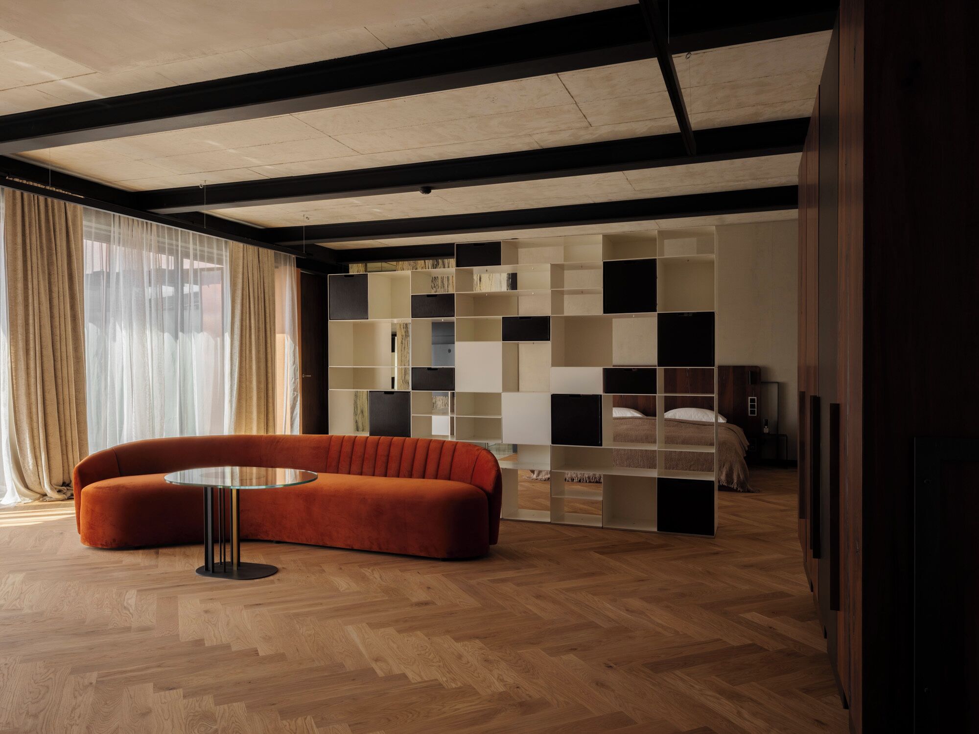 Una habitación moderna con suelo de madera, un sofá, una mesa de vidrio y una estantería empotrada.