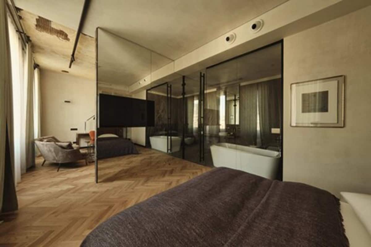 Un dormitorio moderno con una cama grande, un separador de vidrio, una silla y un escritorio.