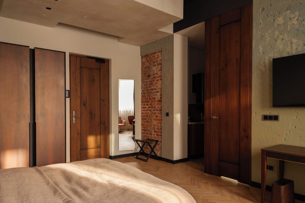 Un dormitorio moderno con una cama grande, armarios de madera, una pared de ladrillo y un televisor montado en la pared.
