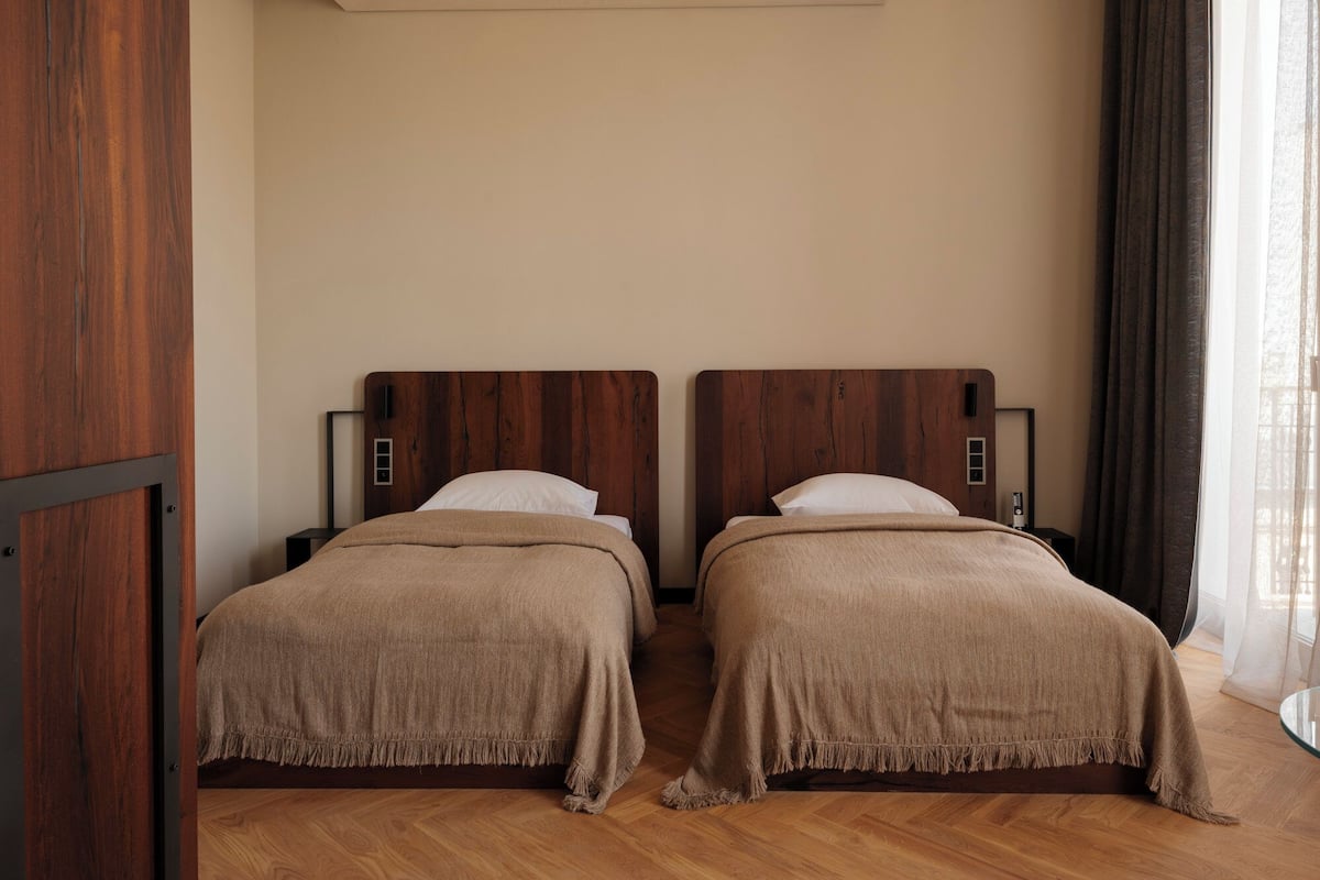 Una habitación con dos camas, cabeceros de madera y un ventanal con cortinas.