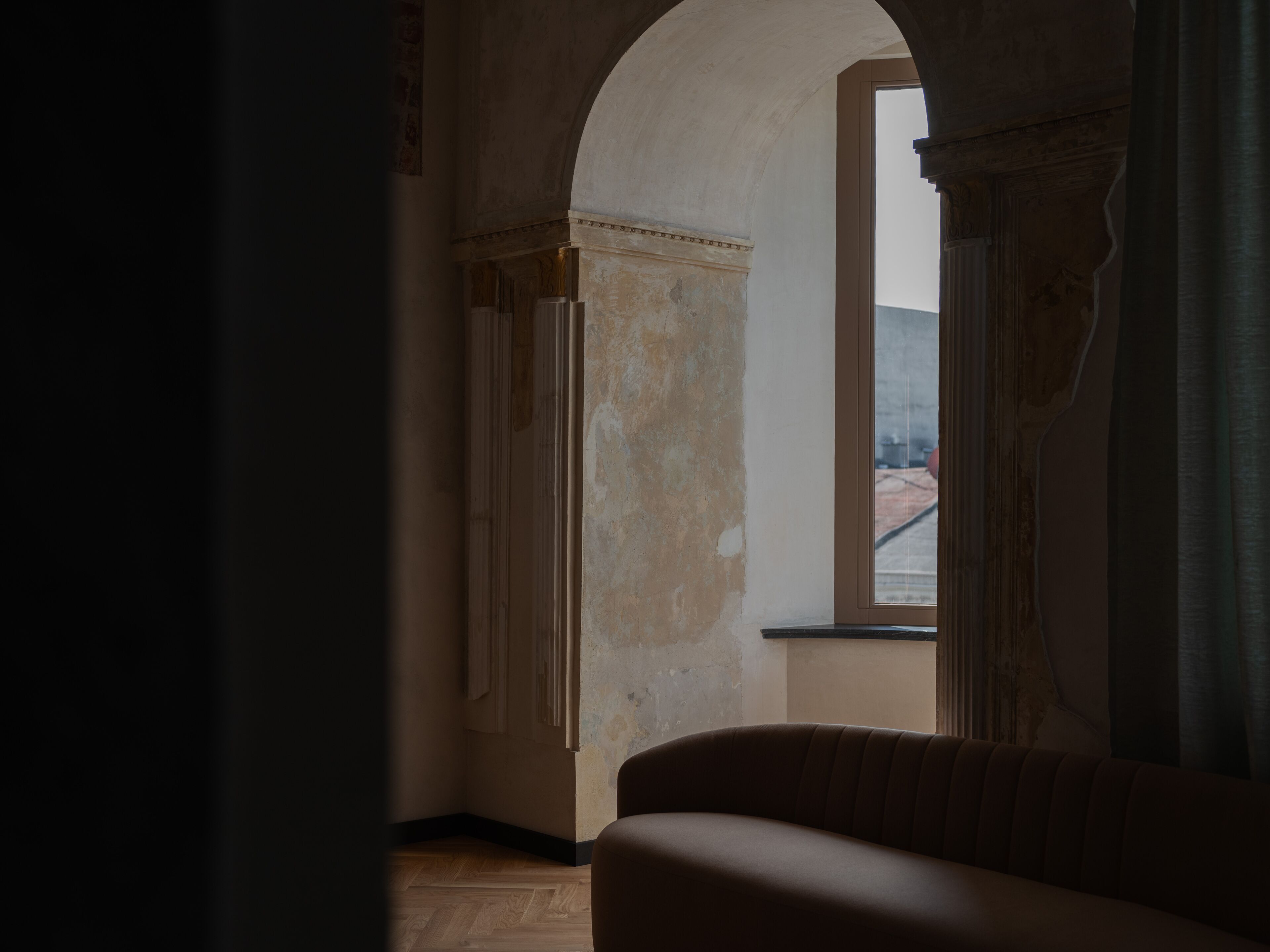 Una habitación tenuemente iluminada, con suelo de madera, un sofá y un arco que da a un espacio exterior.
