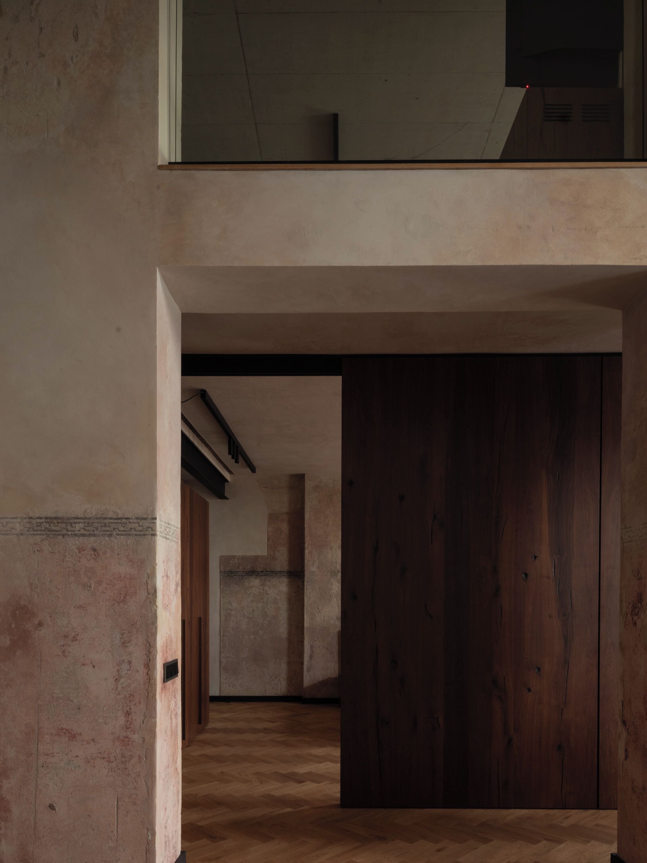 A corridor with wooden flooring and a wooden door at the end.