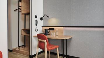 Habitación compacta con escritorio de madera, una silla roja, lámpara de escritorio negra y teléfono en la pared.