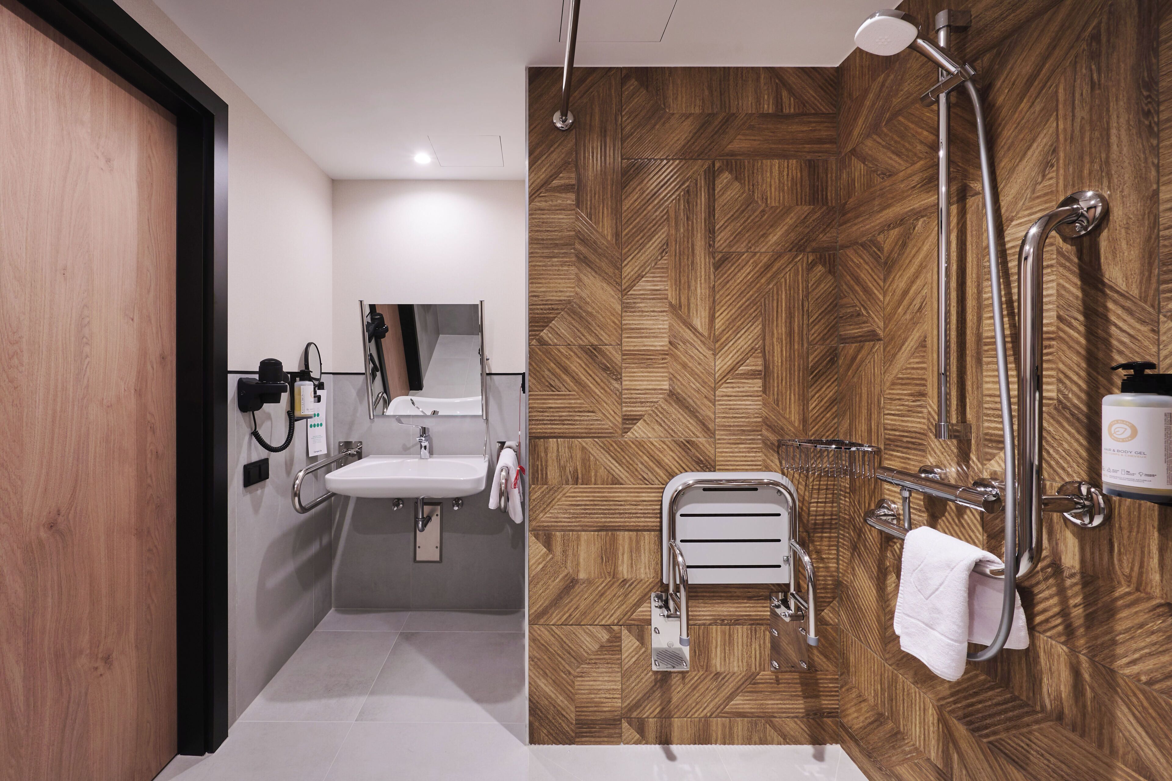 A modern bathroom with a wooden herringbone wall, a sink, a mirror, and a shower with a handheld showerhead.