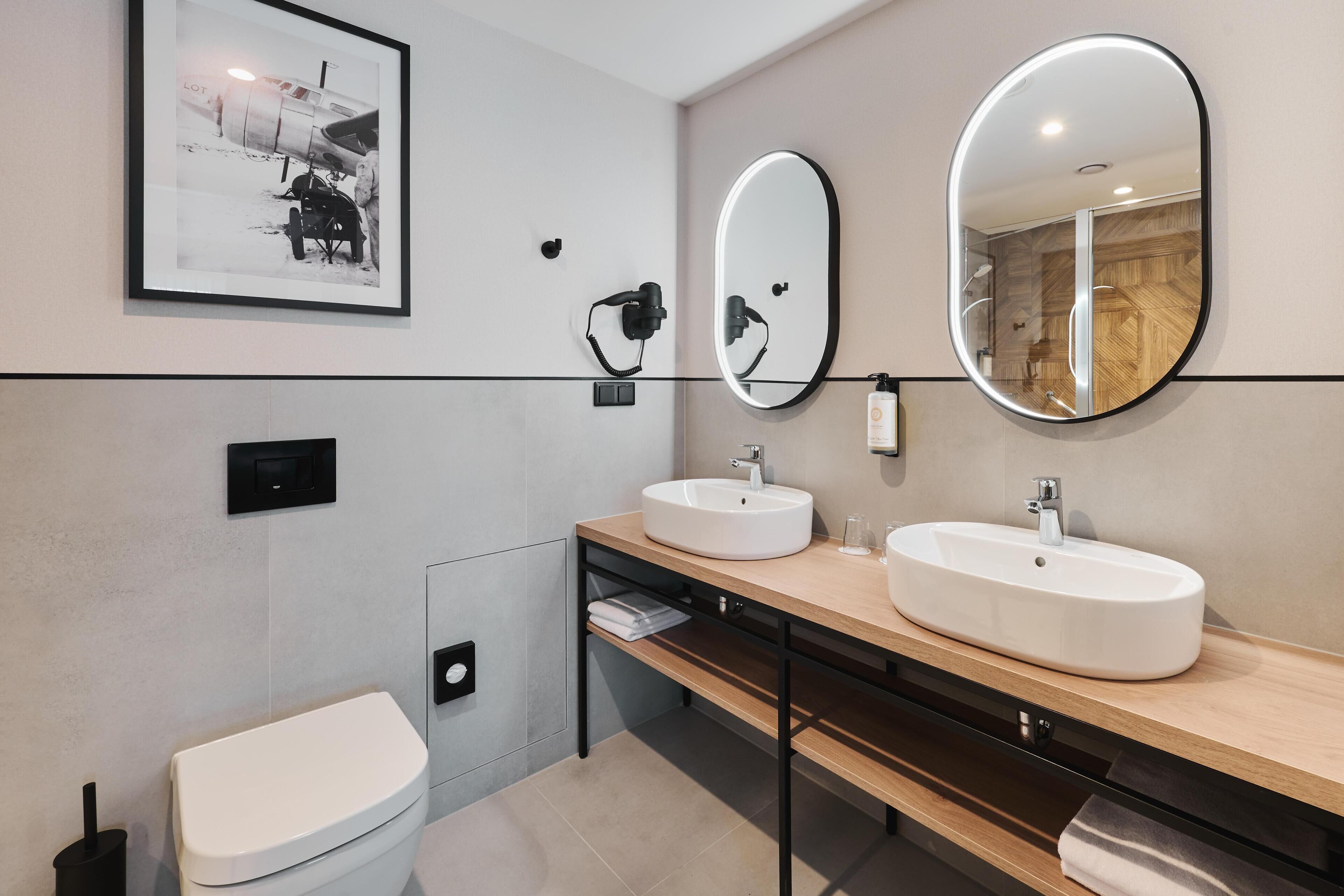 A modern bathroom with two sinks, a toilet, a framed picture, and a mirror.