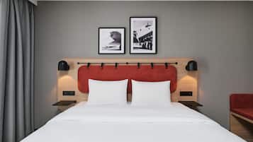 Habitación de hotel con una cama, dos cuadros en la pared, cabecera roja y una silla roja.
