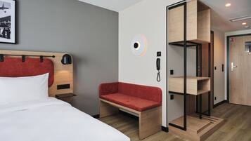 A modern hotel room with a bed, a red sofa, a wooden shelf unit, and a framed picture on the wall.