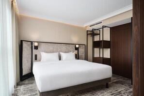 Una habitación de hotel moderna con una cama grande, cabecera con iluminación integrada, armario empotrado y piso alfombrado.