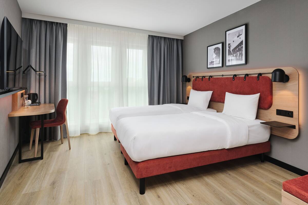 A hotel room with a bed, a desk, a chair, a TV, and curtains.