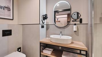 A modern bathroom with a white sink, a large mirror, a handheld phone, and a framed picture on the wall.