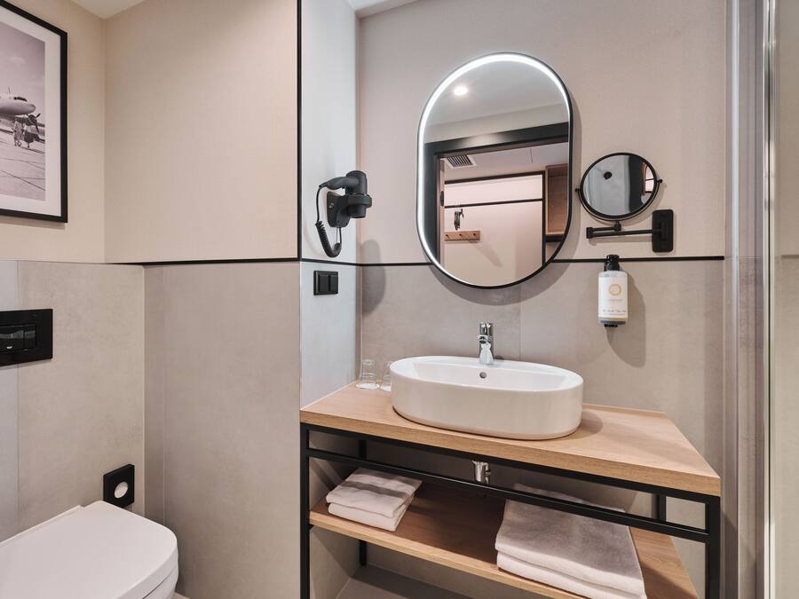 A modern bathroom with a white sink, a large mirror, a handheld phone, and a framed picture on the wall.