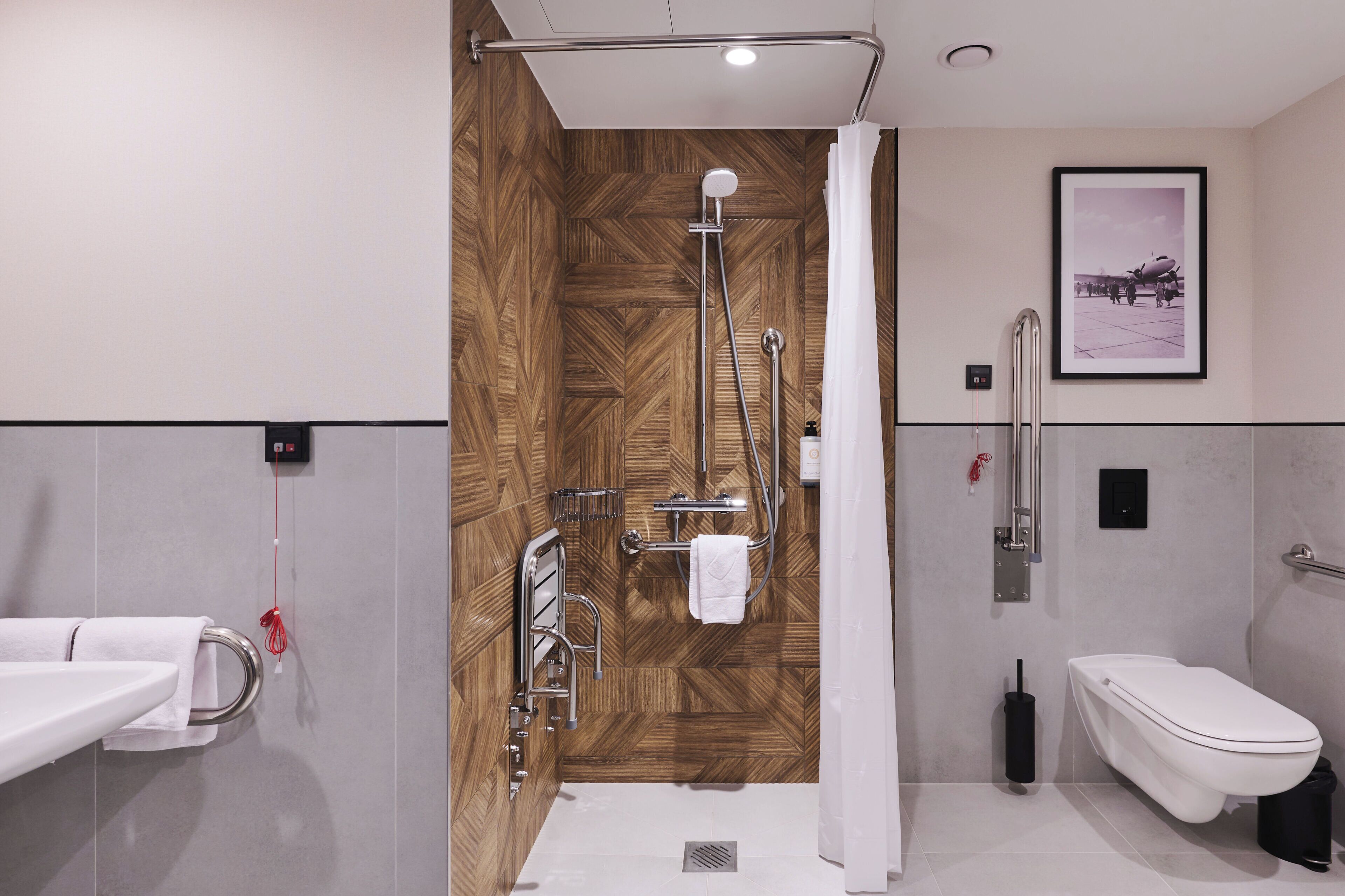 A modern bathroom with a shower, toilet, and sink, featuring a wooden wall panel and a framed picture on the wall.