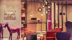 Um saguão de hotel com parede de tijolos, balcão de recepção e mobiliário moderno, incluindo cadeiras vermelhas e roxas.
