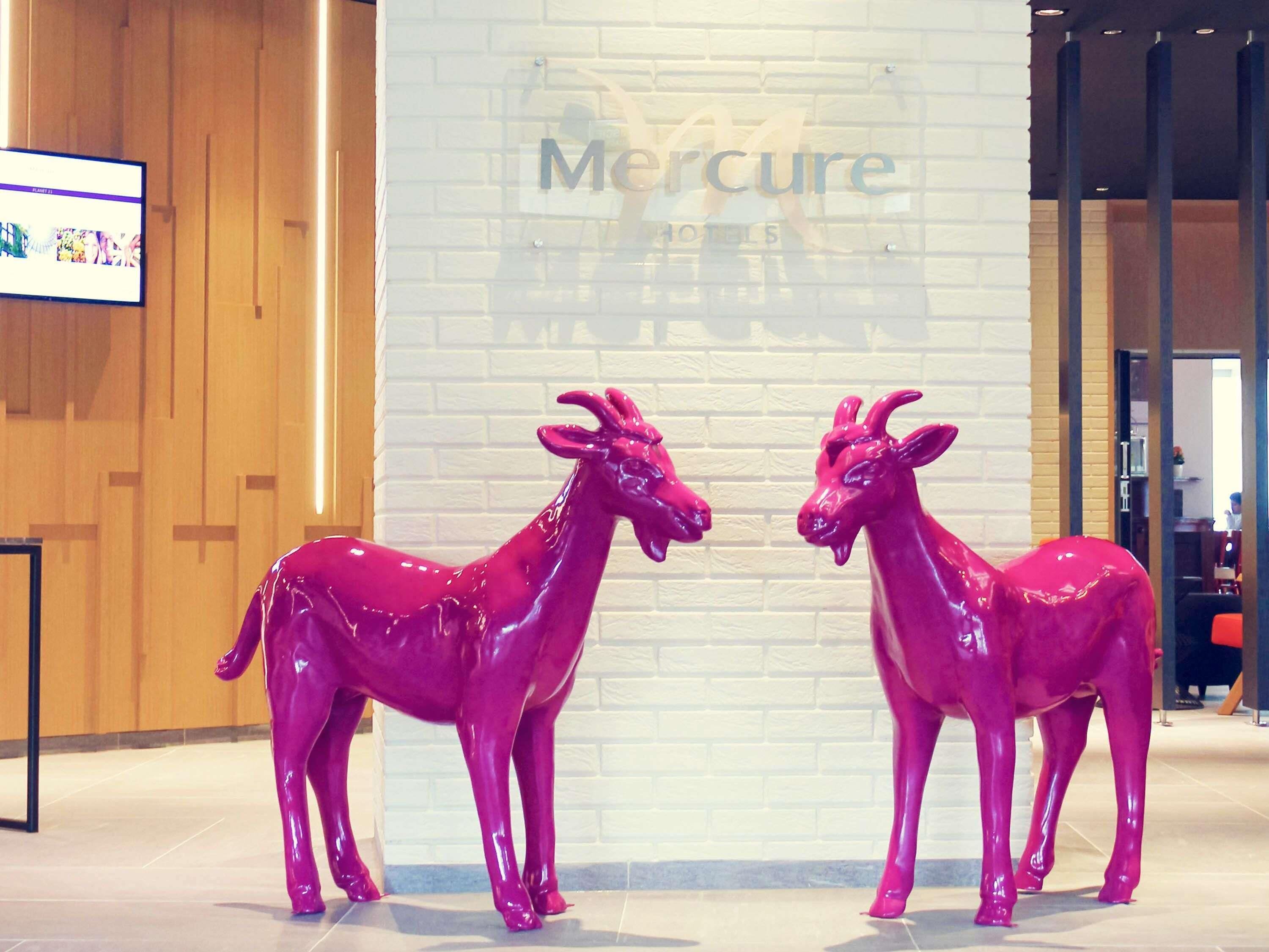 Dos estatuas de burros rosas frente al cartel de un hotel Mercure.