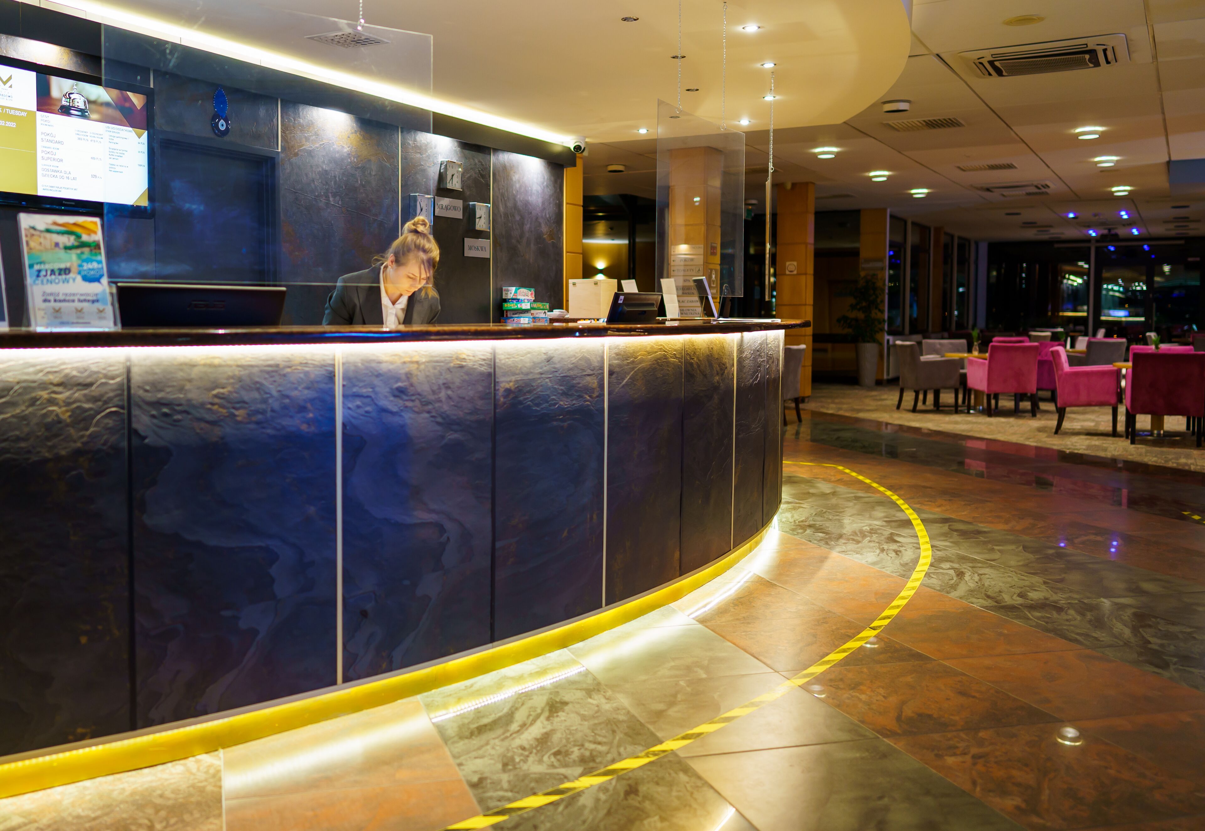 Un espace d’accueil d’hôtel avec un comptoir incurvé, un ordinateur portable et un tableau affichant le menu.