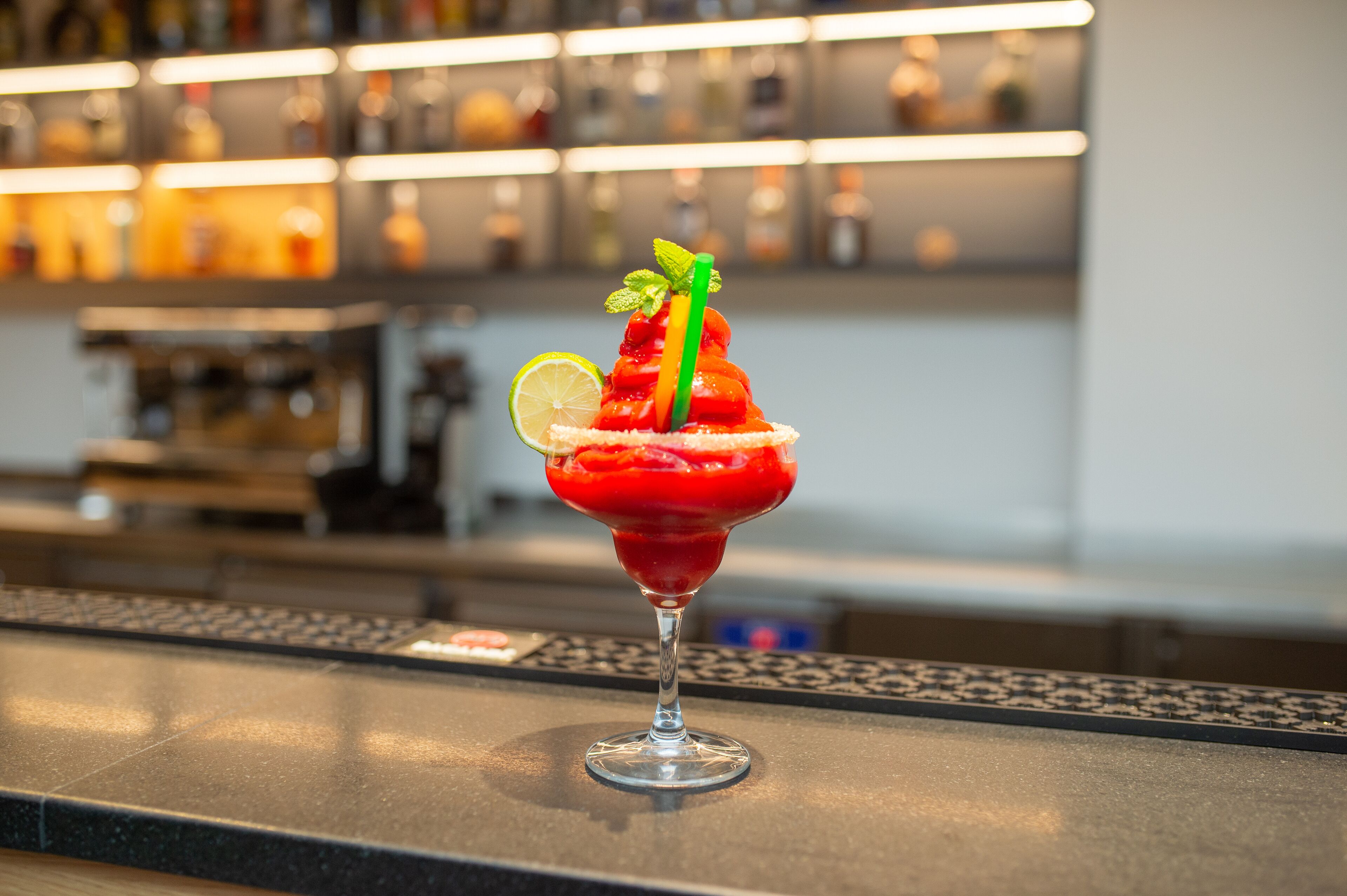 Ein Cocktail mit Limettenspalte und Minzzierde auf einer Bar.