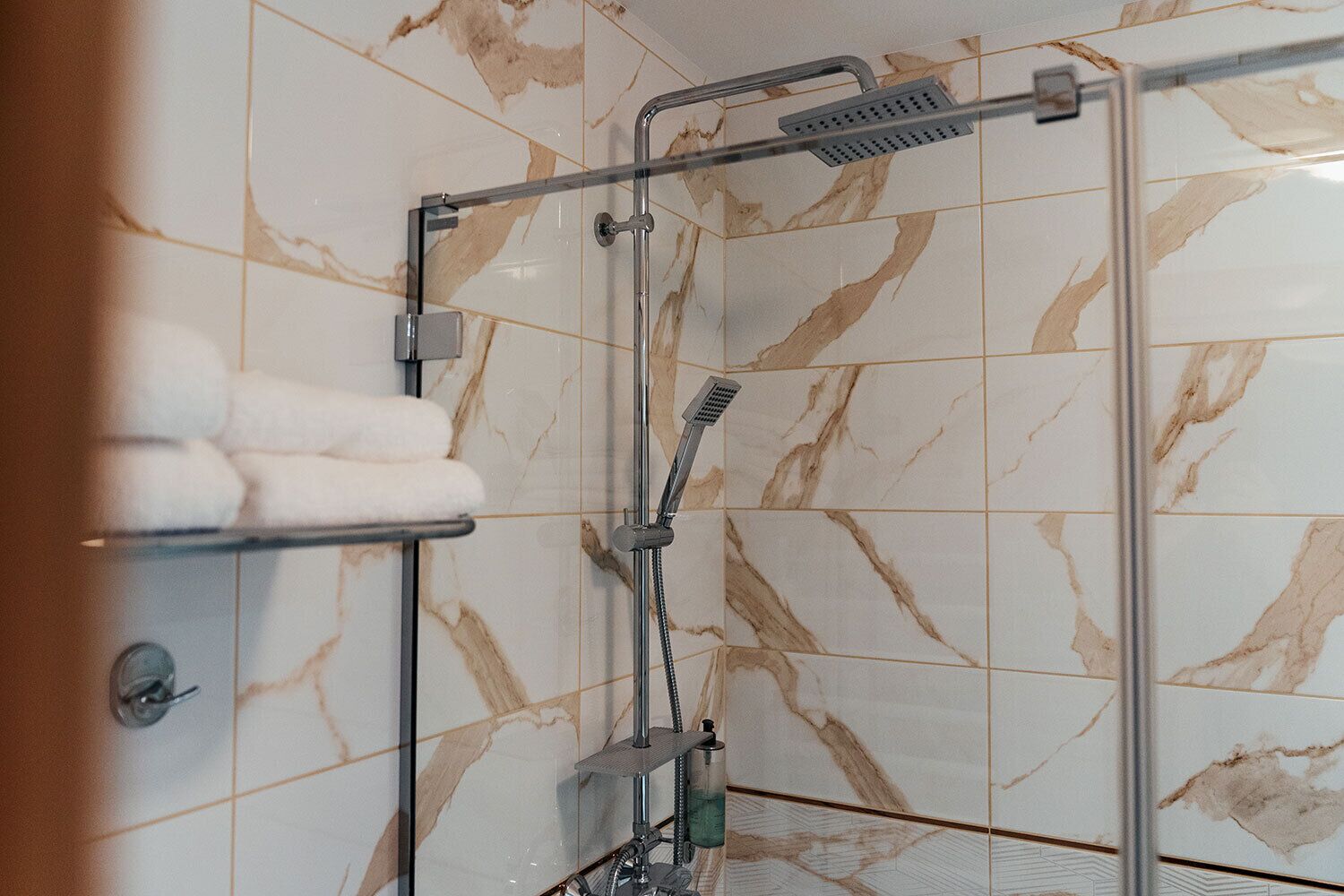 Un área de ducha con puerta de vidrio, un perchero con toallas y un cabezal de ducha manual.
