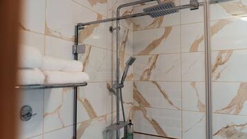 Un área de ducha con puerta de vidrio, un perchero con toallas y un cabezal de ducha manual.