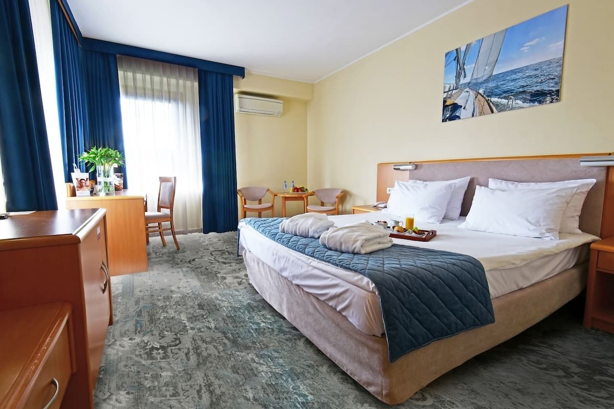 A hotel room with a large bed, a desk, a chair, a small table, and a painting on the wall.