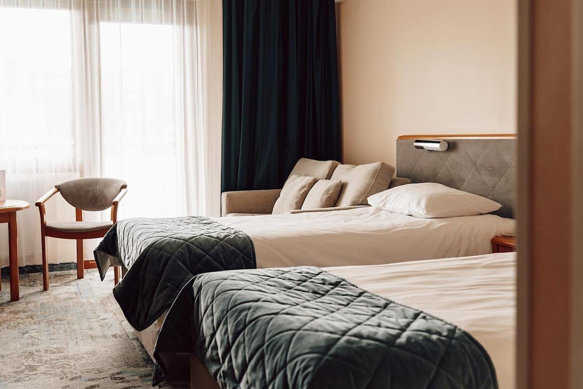 A hotel room with two beds, a chair, and a bedside table.