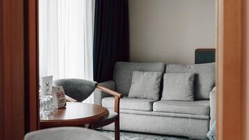 Una habitación de hotel moderna con un sofá gris, una silla de madera y una pequeña mesa redonda.